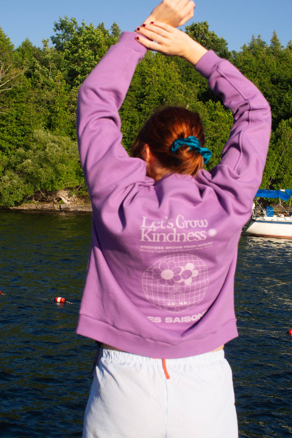Person wearing a purple hoodie with 'Let's Grow Kindness' text by a body of water.