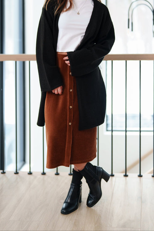 Jupe midi velours côtelé cognac portée avec un cardigan noir et des bottines
